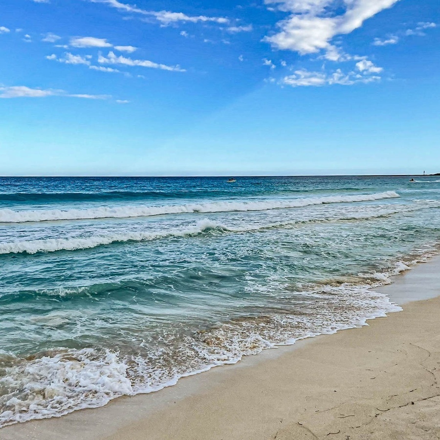 waves crashing on a sandy beach with a boat in the distance