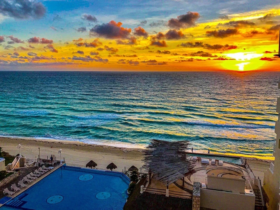 a sunset over the ocean with a swimming pool in the foreground