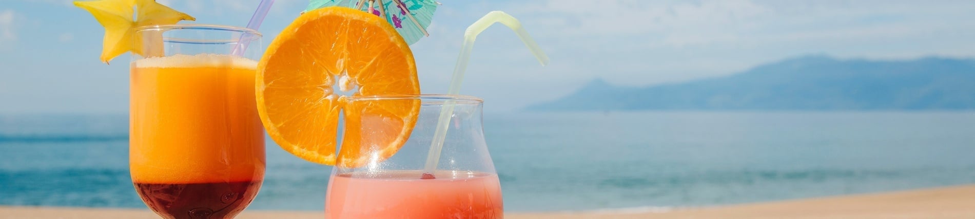 two drinks with straws and slices of fruit on the beach