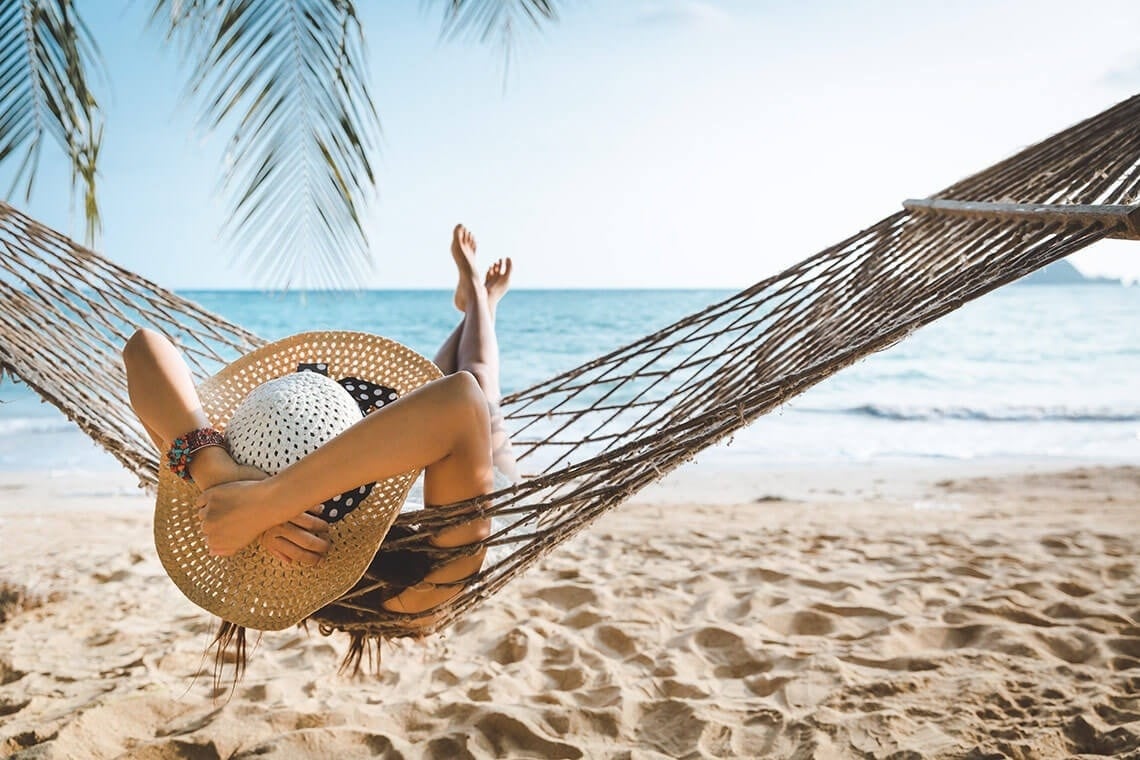 a woman in a hat is laying in a hammock on the beach