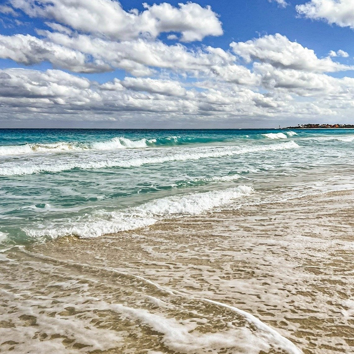 waves crashing on a sandy beach under a cloudy sky
