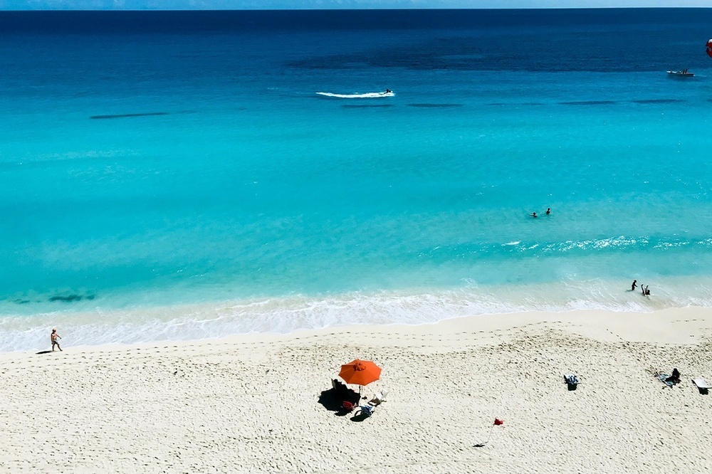 a person sitting under an orange umbrella on a beach