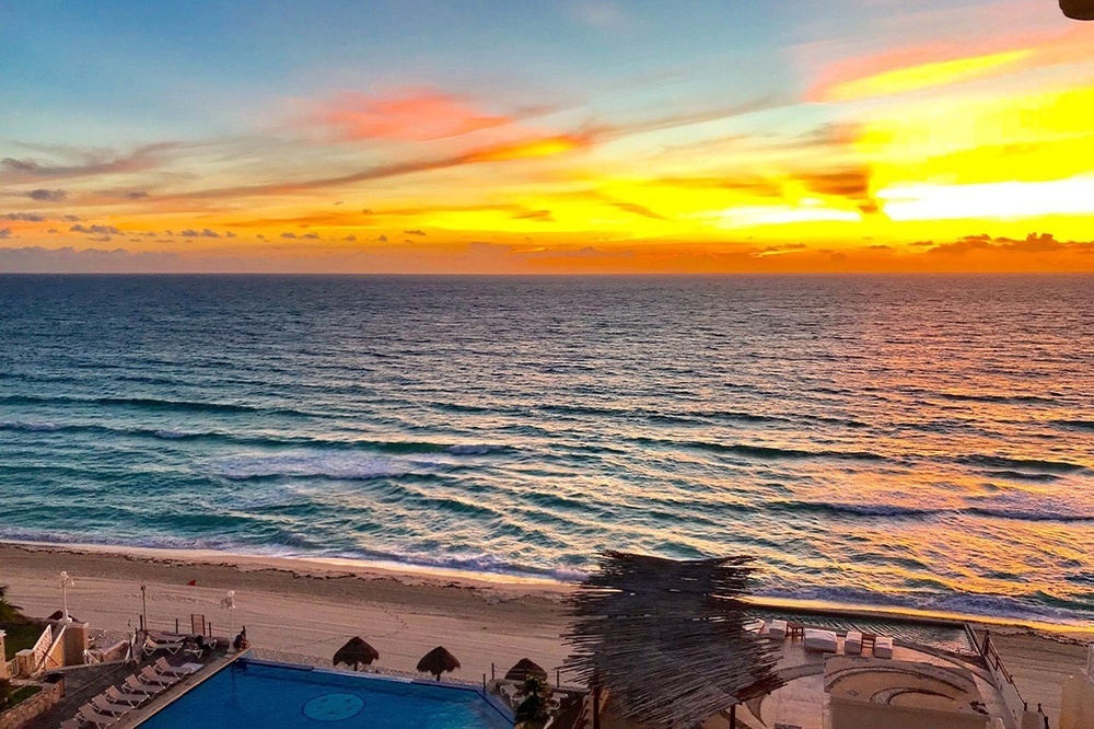 a sunset over the ocean with a swimming pool in the foreground