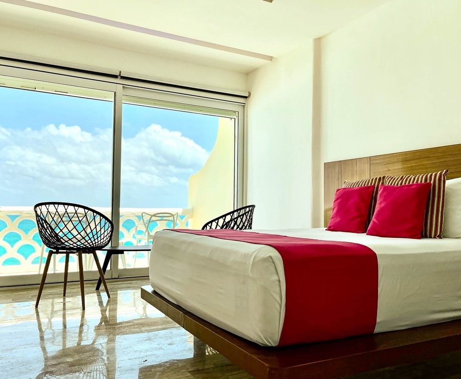 a hotel room with a bed and chairs with a view of the ocean
