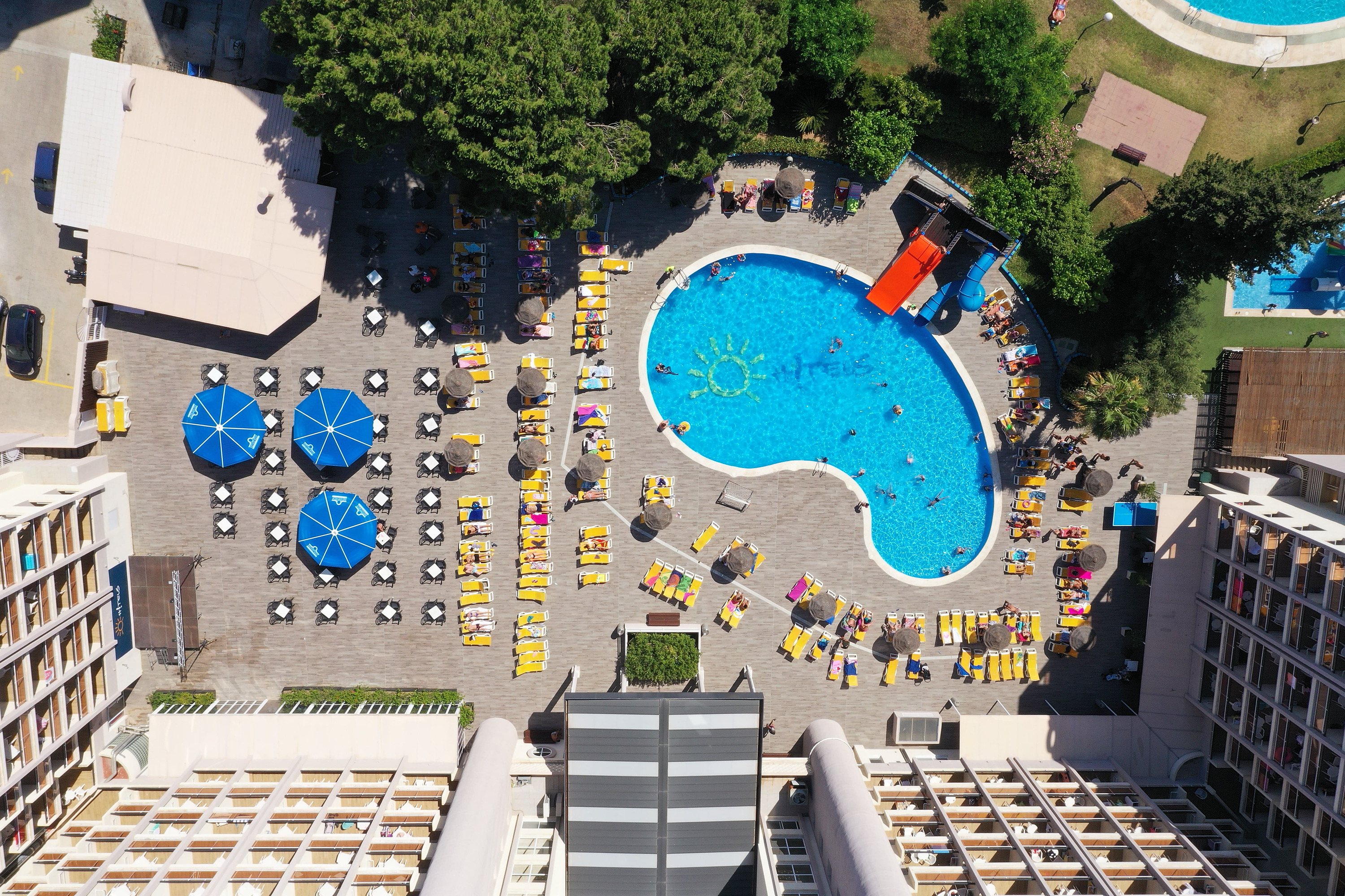 Aerial view of a resort pool with sunbathers and lounge chairs, offering a perfect holiday experience. Hotel near Port Aventura, Salou | Ohtels Belvedere