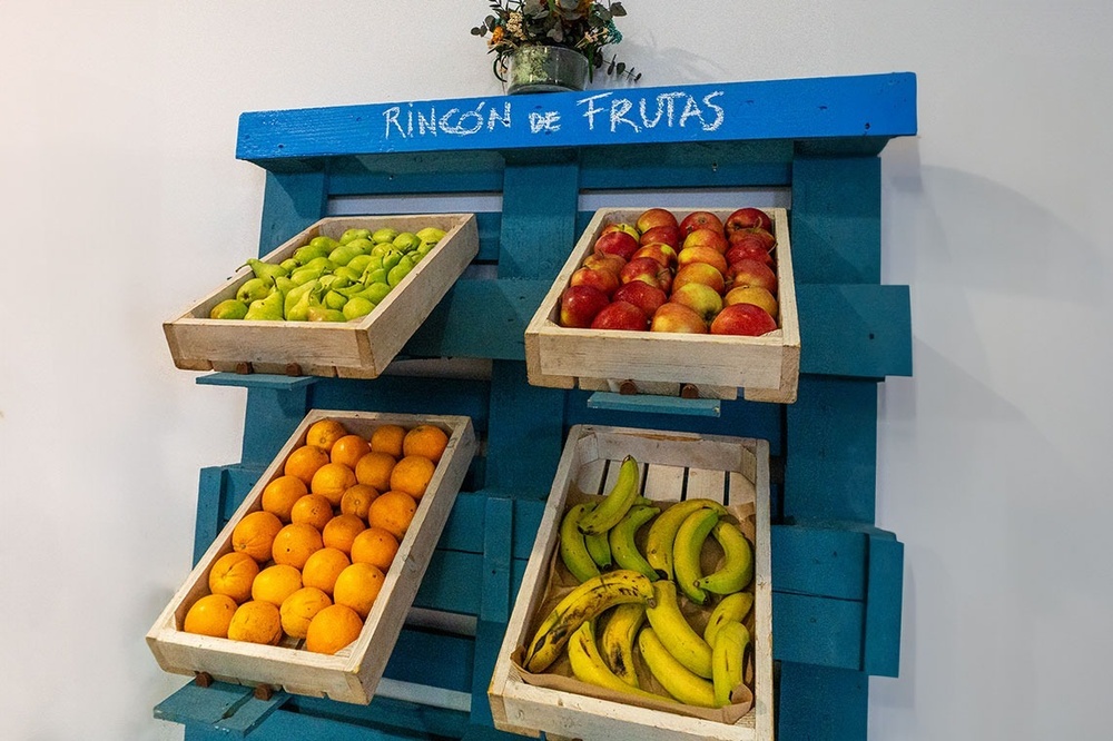un estante de madera con cajas de frutas y una pizarra que dice rincón de frutas