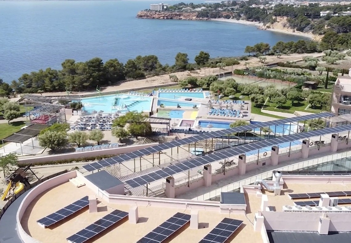 La imagen muestra la moderna entrada de cristal del Gran Hotel Almería, flanqueada por plantas en macetas y con una fachada de azulejos grises.