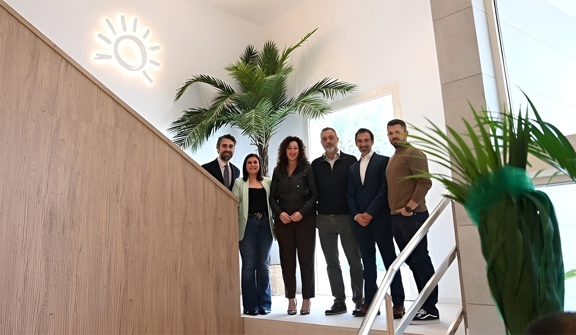 La imagen muestra la moderna entrada de cristal de un edificio con el letrero "GRAN HOTEL ALMERIA" en su fachada de azulejos grises, flanqueada por plantas en macetas.