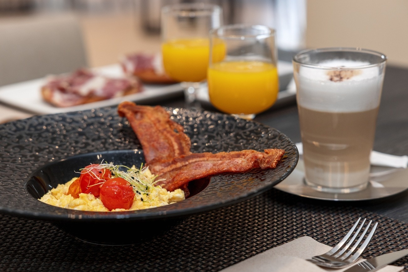 un plato de huevos revueltos con tocino y tomates junto a un vaso de café