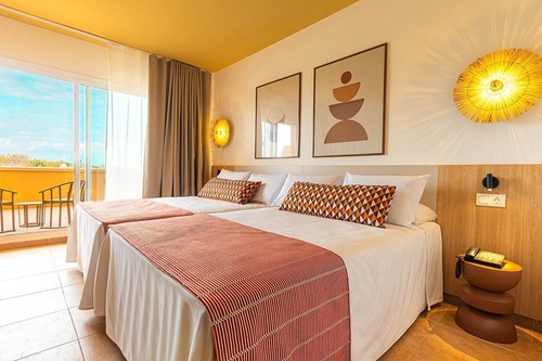 Luminosa habitación de hotel con dos camas individuales, balcón, techo amarillo y decoración moderna en tonos cálidos.