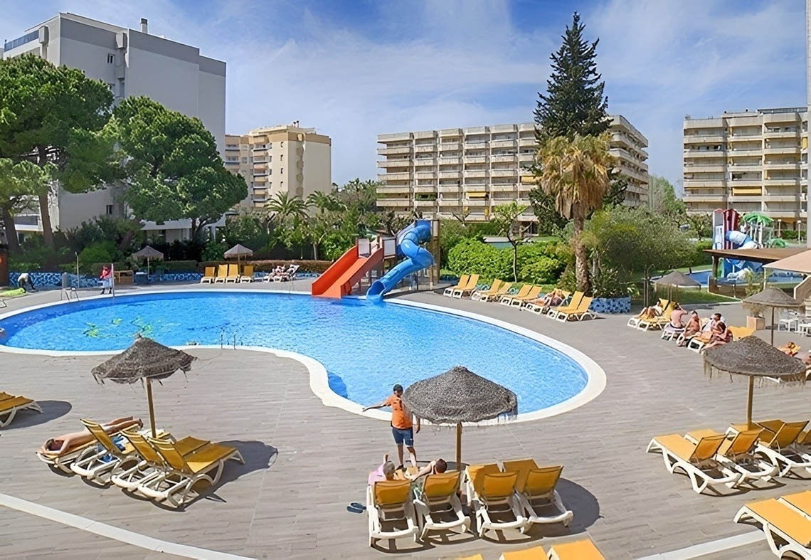 La imagen muestra la moderna entrada de cristal de un edificio con el letrero "GRAN HOTEL ALMERIA" en su fachada de azulejos grises, flanqueada por plantas en macetas.