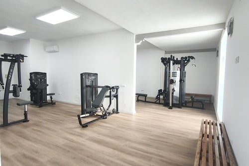 Un gimnasio moderno y luminoso, equipado con varias máquinas de ejercicio, paredes blancas y suelo de madera clara.