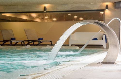 Piscina interior com cascata e espreguiçadeiras no Hotel Vila Romana, perto de Porto Aventura.