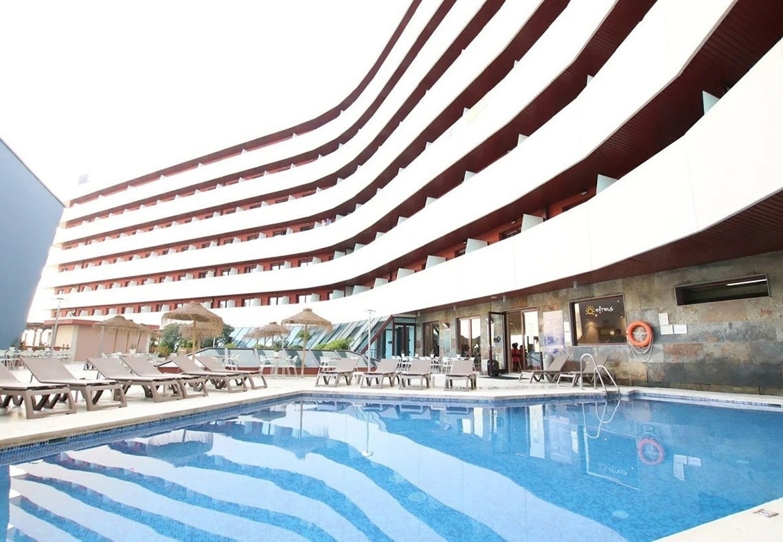 L'image représente l'entrée moderne du Gran Hotel Almeria, avec sa façade en carrelage gris, des portes vitrées et des plantes en pot de chaque côté.