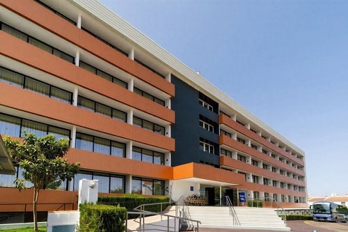 Un moderno edificio de varios pisos con balcones de color terracota y una sección azul oscuro destaca bajo un cielo azul claro.