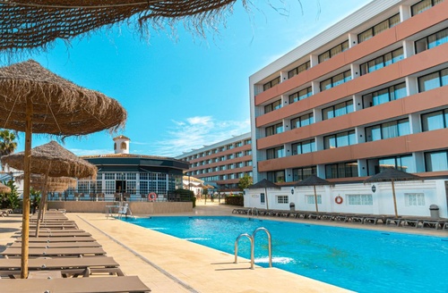 Hotel en Matalascañas: piscina cristalina rodeada de tumbonas y palmeras.