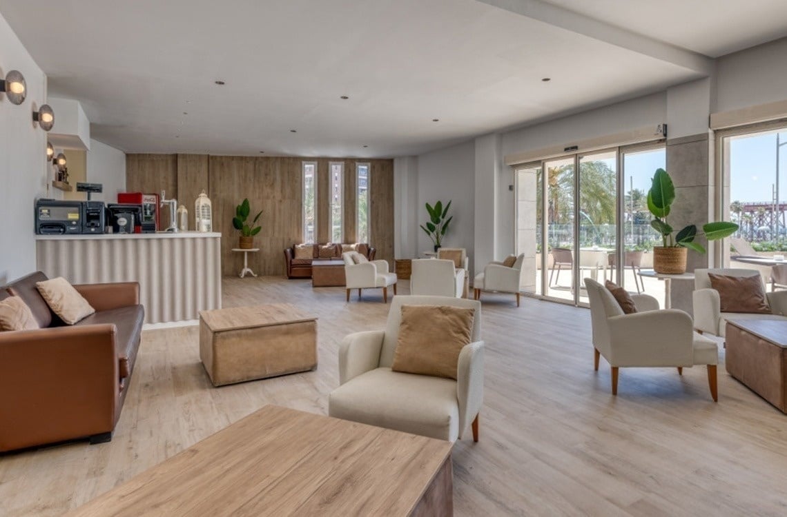 L'image représente l'entrée moderne du Gran Hotel Almeria, avec sa façade en carrelage gris, des portes vitrées et des plantes en pot de chaque côté.
