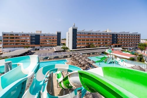 un parque acuático con toboganes verdes y azules frente a un gran edificio