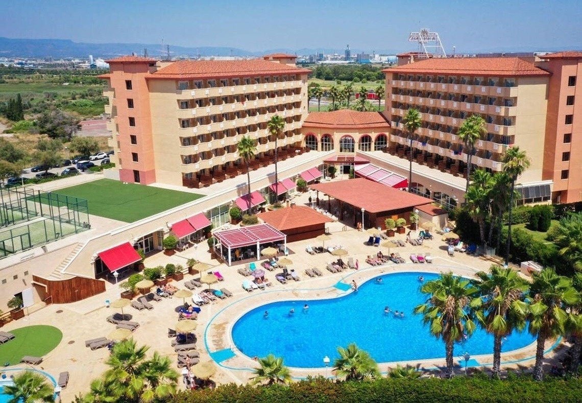 The entrance of the Gran Hotel Almeria is shown with its name prominently displayed above glass doors, flanked by potted plants and set against a light grey tiled facade.
