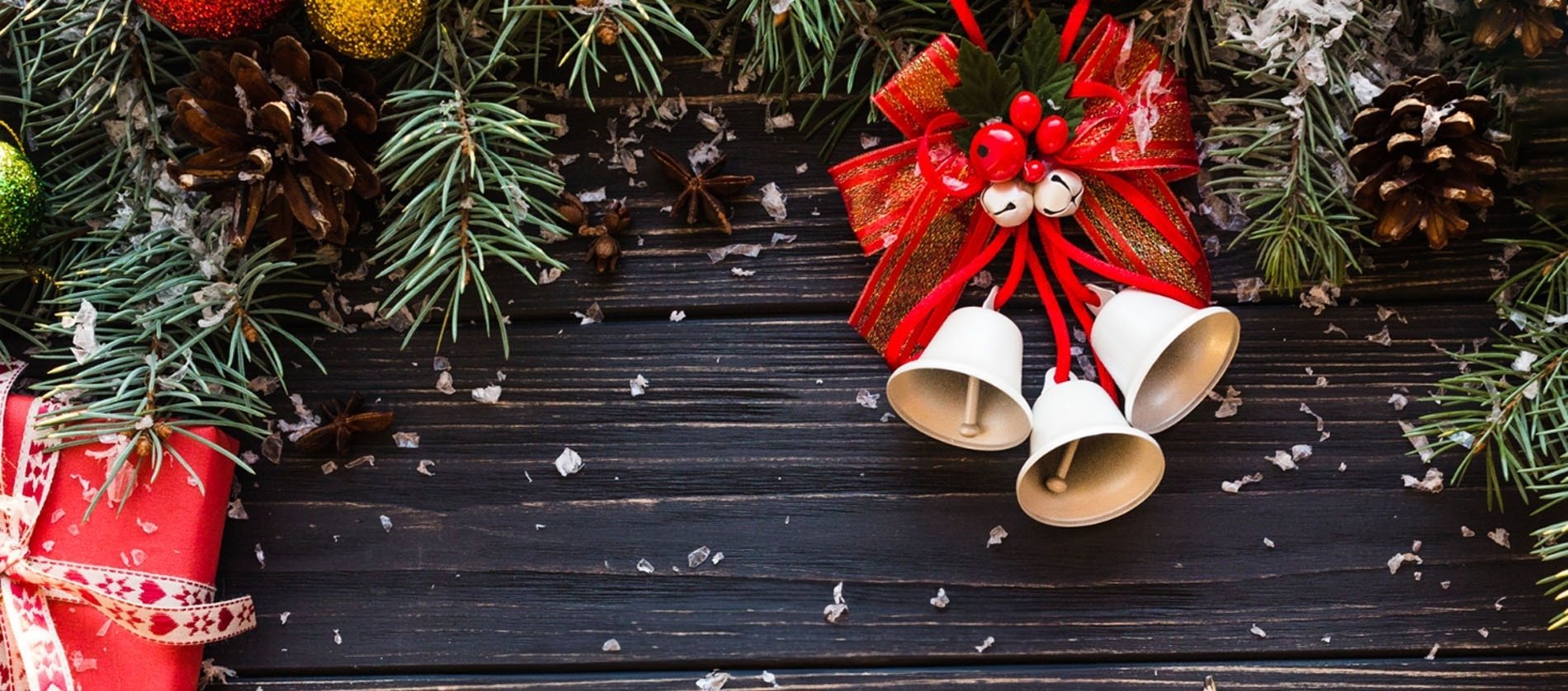 christmas bells hanging from a red ribbon on a wooden table