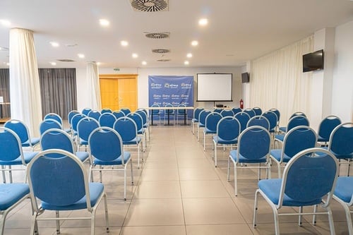 uma sala de conferências com cadeiras azuis e uma tela de projeção