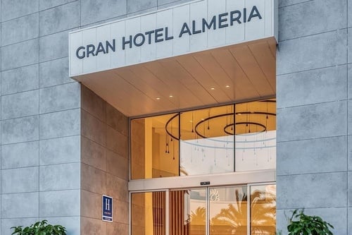 L'image présente l'entrée moderne du Gran Hotel Almeria, identifiable par son enseigne, ses portes vitrées automatiques et sa façade élégante en panneaux.