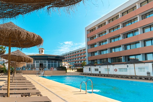 une grande piscine entourée de chaises et d' parasols avec un grand bâtiment en arrière-plan