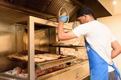 Un cuisinier fait griller du pain sur un four à charbon de bois, ajustant la hauteur de la grille.
