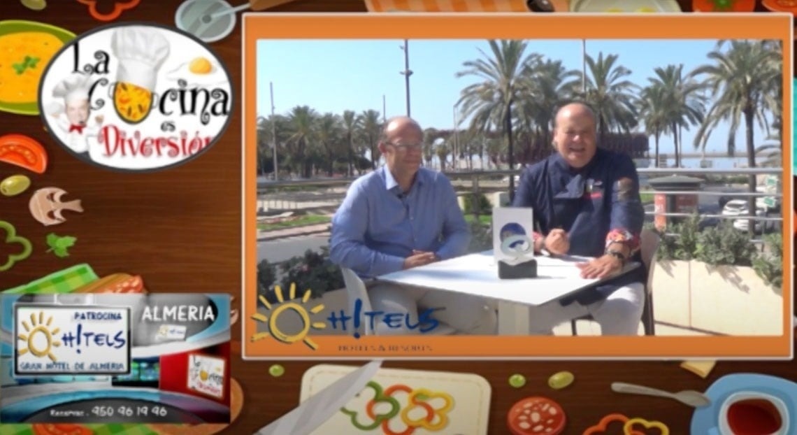 A imagem exibe a fachada moderna da entrada do Gran Hotel Almeria, com paredes de azulejos cinza claro, portas de vidro e vasos com plantas decorativas.