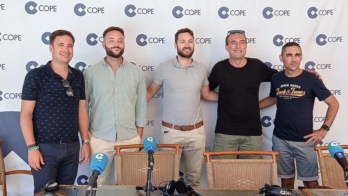 La imagen muestra la moderna entrada de cristal de un edificio con el letrero "GRAN HOTEL ALMERIA" en su fachada de azulejos grises, flanqueada por plantas en macetas.