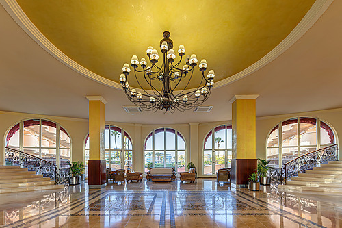 Lustre imponente e teto dourado no lobby de hotel elegante com piso de mármore polido e escadarias. Hotel tudo incluído em La Pineda | Ohtels La Hacienda