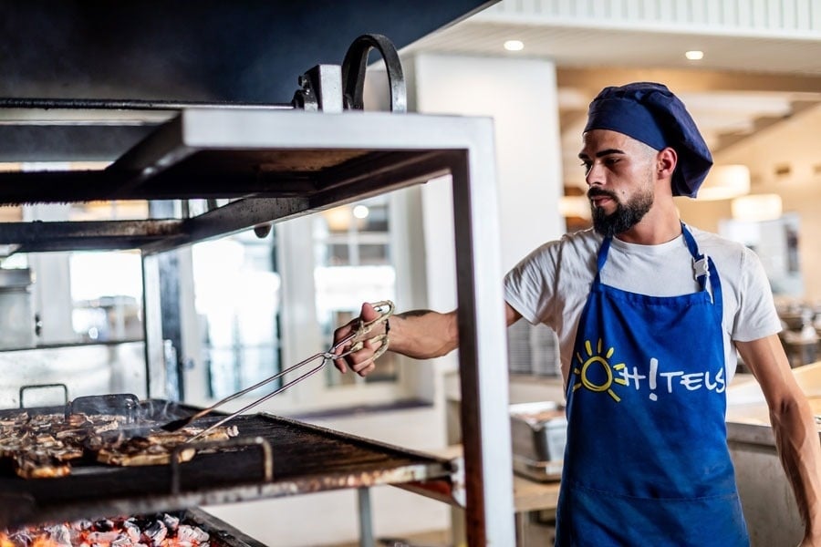 un hombre con un delantal azul y una camisa blanca está cocinando comida en una parrilla