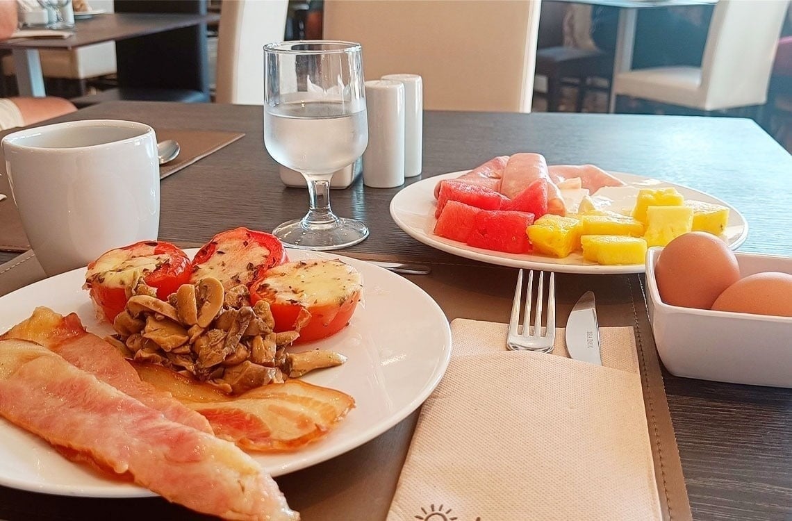 La imagen muestra la moderna entrada de cristal del Gran Hotel Almería, flanqueada por plantas en macetas y con una fachada de azulejos grises.