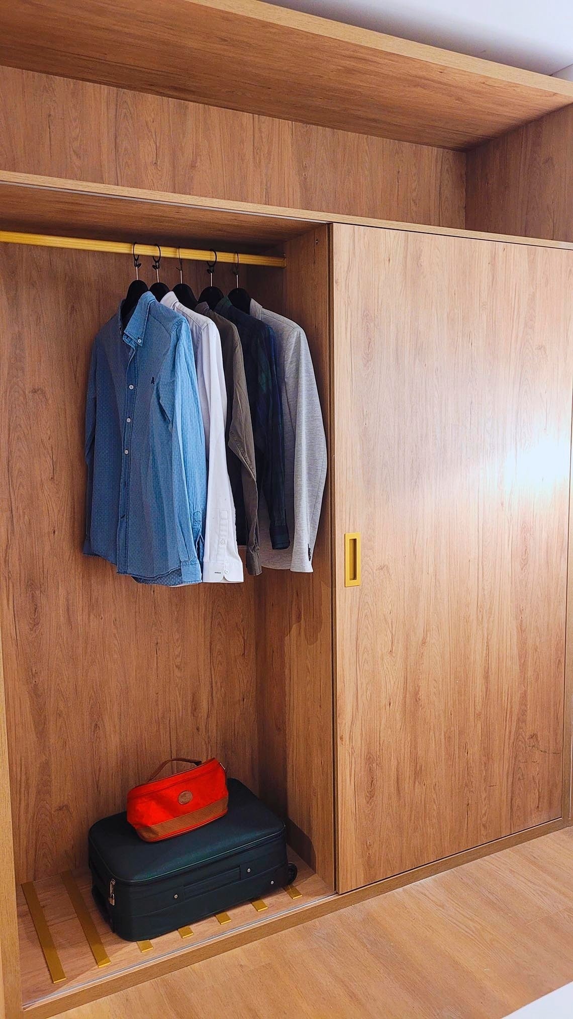 un placard en bois avec des vêtements suspendus et une valise sur le sol