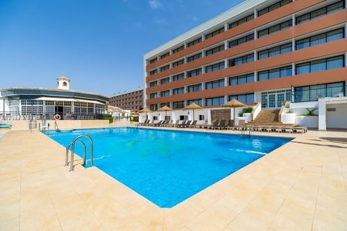 una gran piscina rodeada de sillas y sombrillas frente a un gran edificio