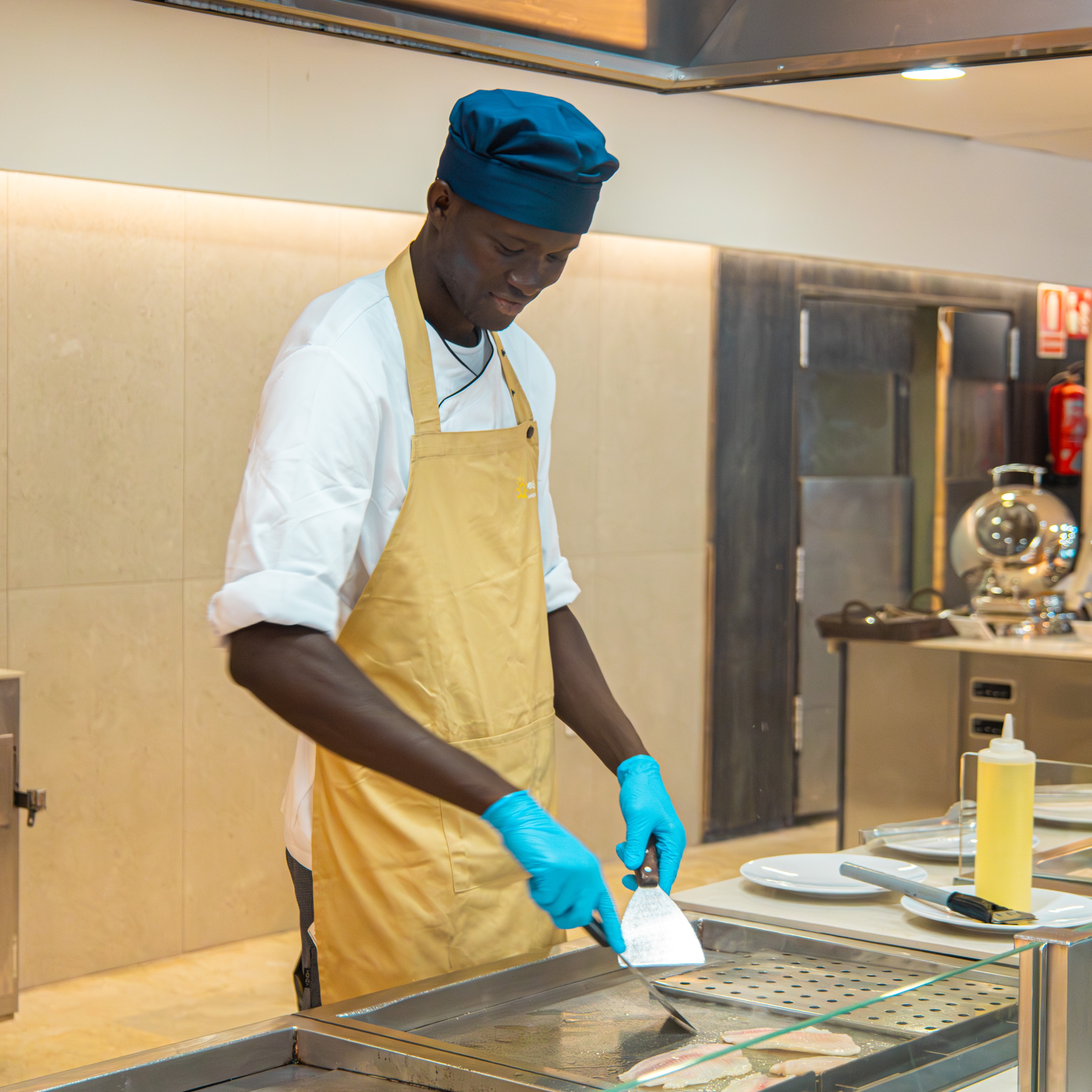 Chef cocina pescado en Ohtels: Corporativa, con gorro azul y delantal.