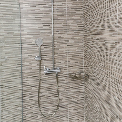 una ducha en un baño con baldosas marrones y blancas