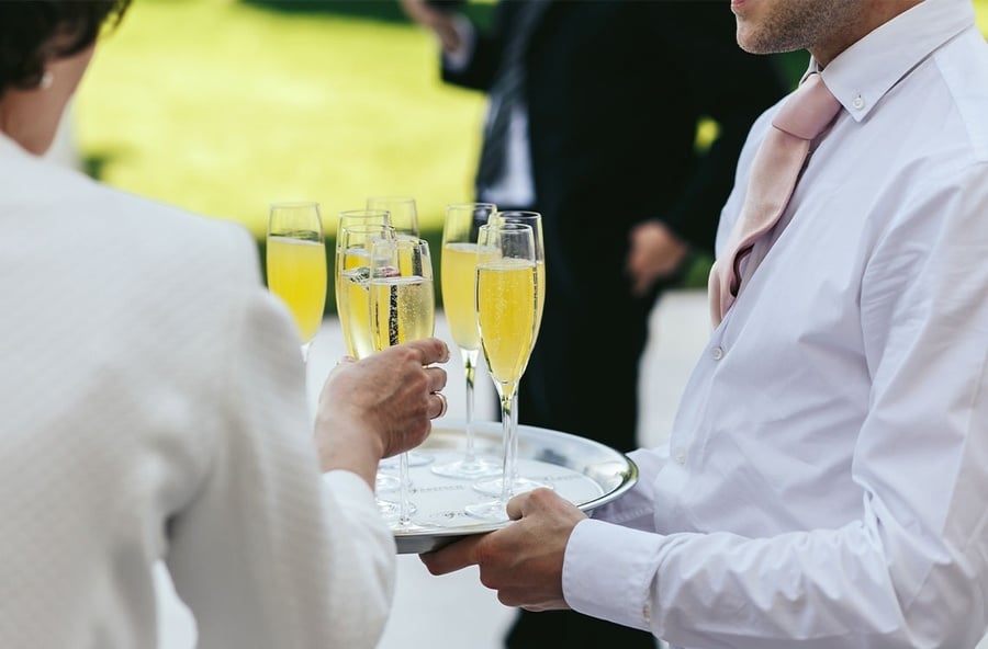 a man in a white shirt is holding a tray of champagne glasses