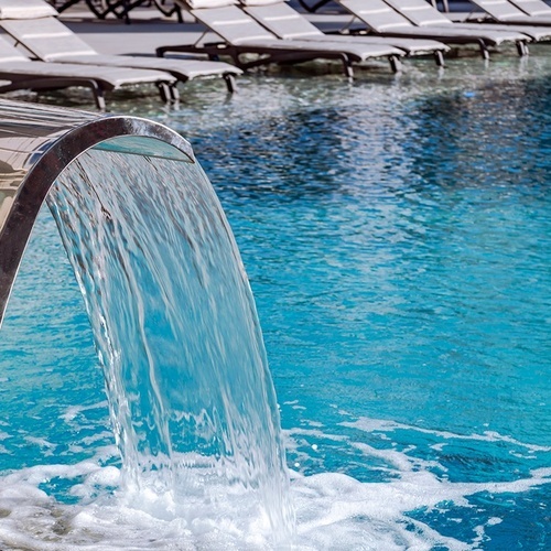 una cascada en una piscina con sillas de playa en el fondo