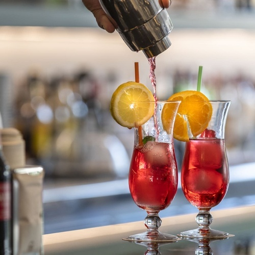 un barman vierte un cóctel rojo en un vaso con una pajita