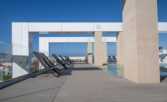 a row of chairs sit on a rooftop deck overlooking a swimming pool