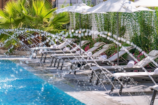 a row of lounge chairs next to a pool with a fountain spraying water