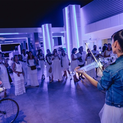 una mujer con una chaqueta de mezclilla y un vestido blanco toca un violín