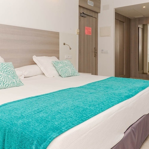 una habitación de hotel con una cama blanca y una manta turquesa