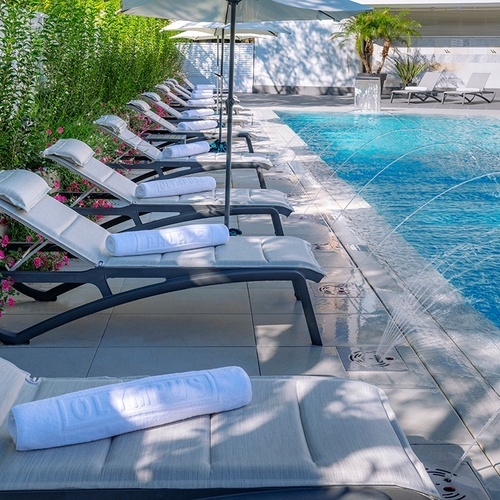 una fila de tumbonas con toallas y sombrillas junto a una piscina