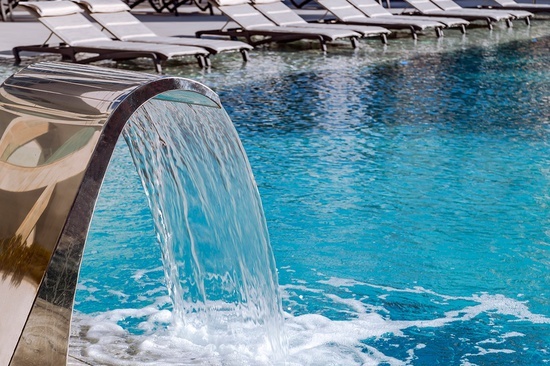 a waterfall in a swimming pool with chairs in the background