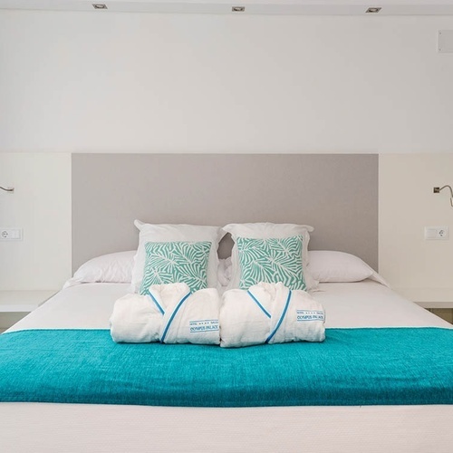 una cama blanca con una manta turquesa y dos almohadas