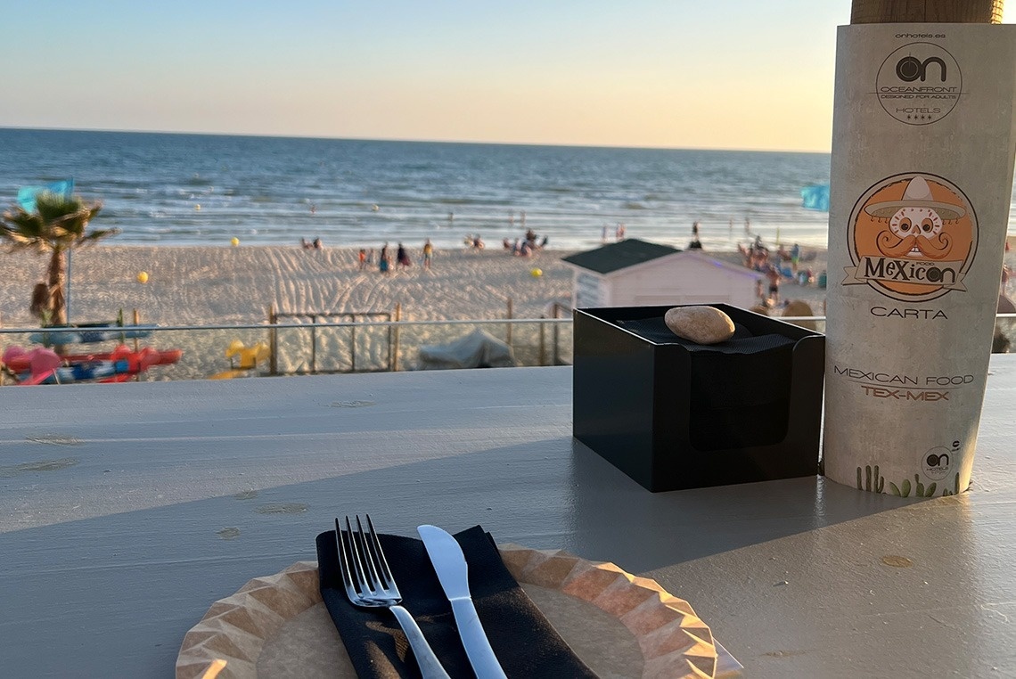a mexican food menu sits on a table in front of a beach