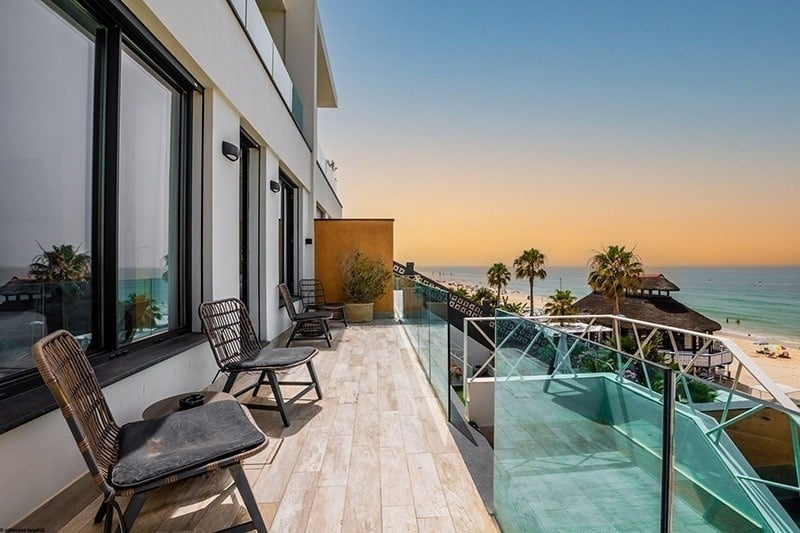 a balcony with chairs and a glass railing overlooking the ocean