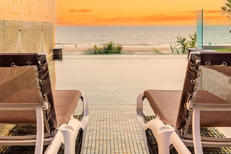 two lounge chairs are sitting next to a swimming pool overlooking the ocean